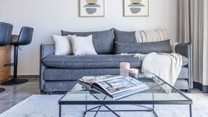 A modern living room with a grey sofa, a glass coffee table, and two abstract paintings on the wall. - Fantastic 1 Bedroom In City Center - isrentals (Jerusalem)