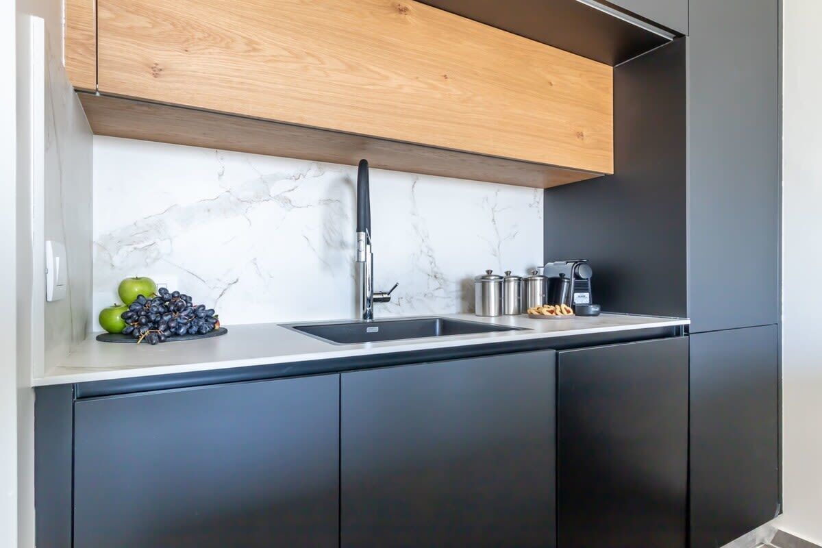 Une cuisine moderne avec un dosseret en marbre, un meuble supérieur en bois, un évier noir et des appareils électroménagers en acier inoxydable.