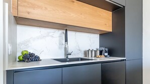 A modern kitchen with a marble backsplash, a wooden upper cabinet, a black sink, and stainless steel appliances. - Fantastic 1 Bedroom In City Center - isrentals (Jerusalem)