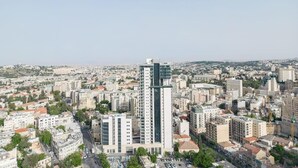 A high-rise building with a modern design, surrounded by a dense urban area with various other buildings. - Fantastic 1 Bedroom In City Center - isrentals (Jerusalem)