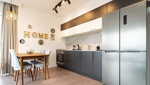 A modern kitchen with a dining area, featuring stainless steel appliances, grey cabinetry, and a wooden dining table with chairs. - 1 Bedroom Savyon View - Isrentals (Jerusalem)
