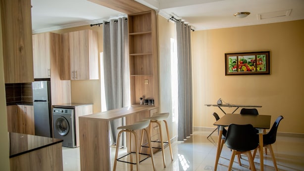 A modern kitchen with wooden cabinets, a washing machine, a bar area, and a dining table with chairs. - The Backyard Lodge (Mpingu)