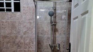 A bathroom with a glass-enclosed shower, a toilet, and a door. - The Backyard Lodge (Mpingu)