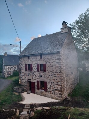 Un bâtiment en pierre avec un toit en pente, une cheminée et un petit porche.