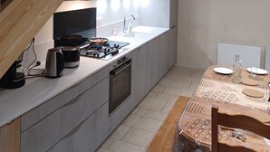 A modern kitchen with a built-in oven, microwave, and sink. There is a wooden dining table with chairs and a decorative bottle. - Maison Restaurée: "lou Cantou des Randonneurs", Proche de Sentiers de Randonnées (chavagnac)