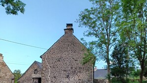 A rustic stone building with a chimney, surrounded by greenery and a swing set. - Maison Restaurée: "lou Cantou des Randonneurs", Proche de Sentiers de Randonnées (chavagnac)