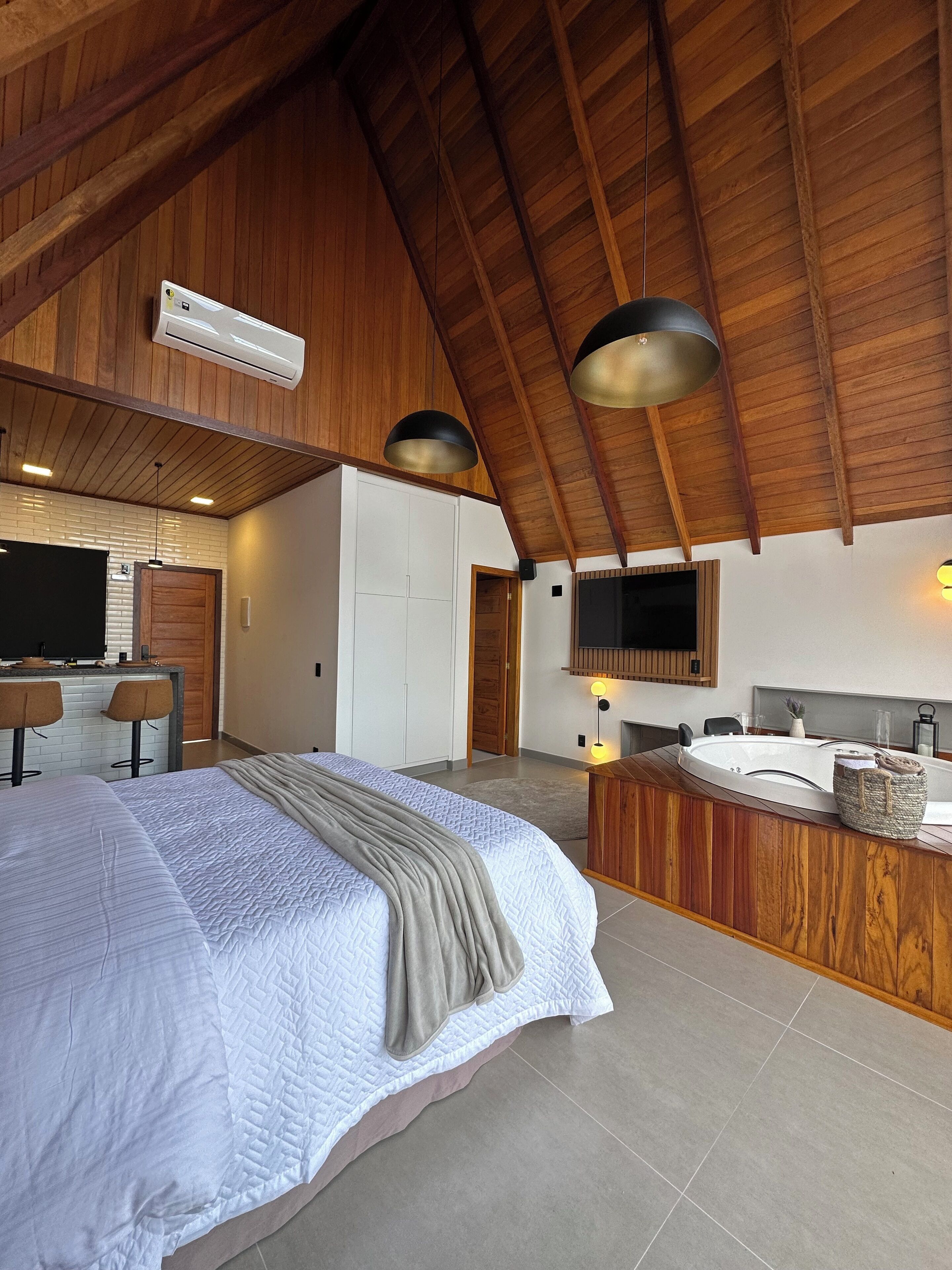 A spacious bedroom with a large bed, a wooden ceiling, and a modern bathroom with a vanity and sink.