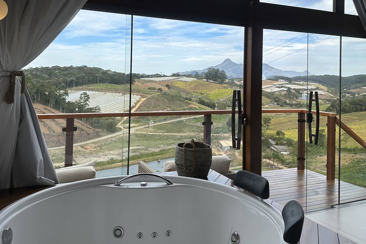 A large, modern bathroom with a bathtub, a view of a scenic landscape through large windows, and a wooden deck outside.