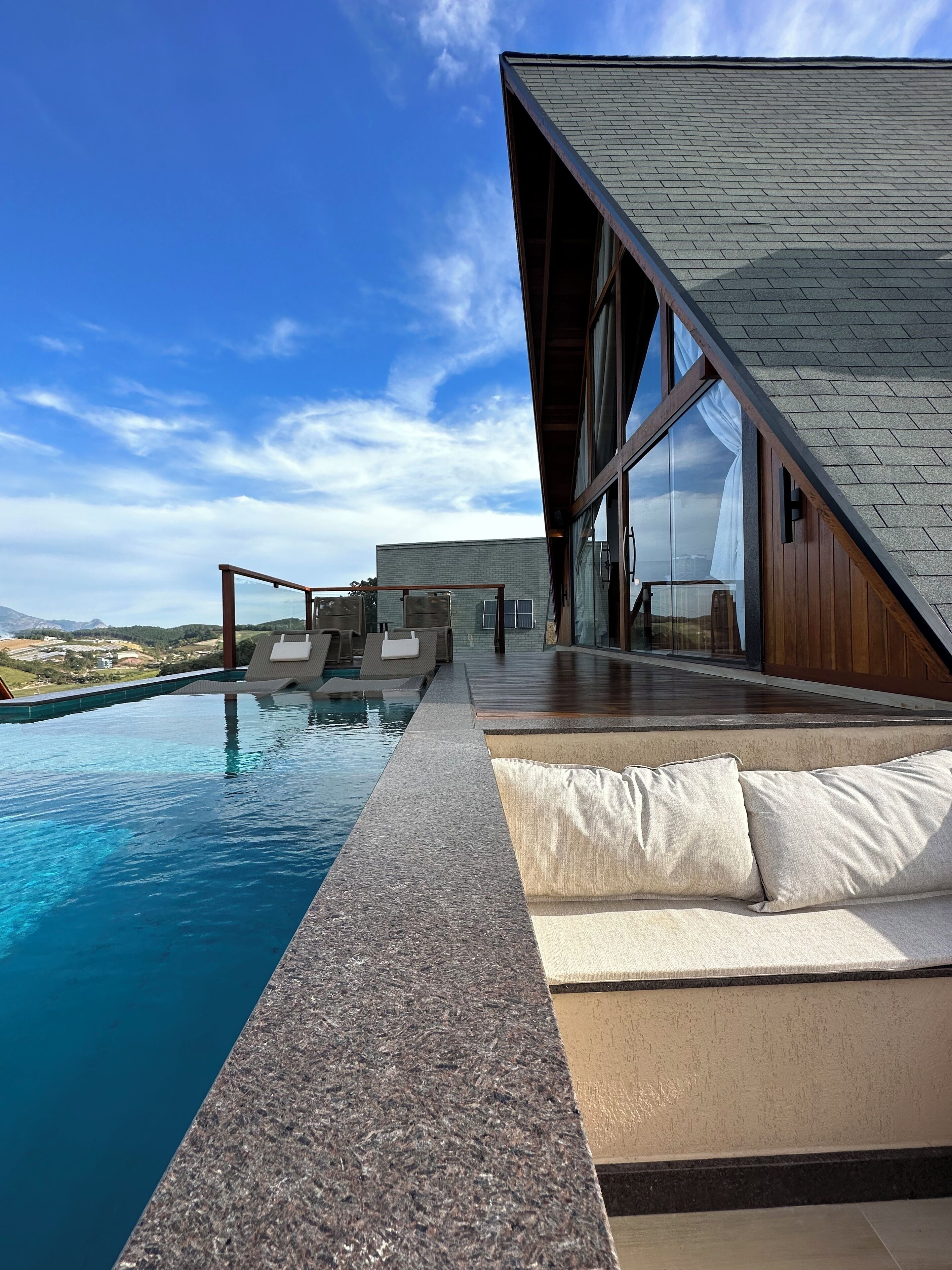 Ein moderner Poolbereich im Freien mit freiem Blick auf die umliegende Landschaft, einer Holzterrasse und einem großen Panoramafenster.