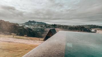 Une piscine offrant une vue sur un paysage vallonné, avec une structure en bois en arrière-plan.