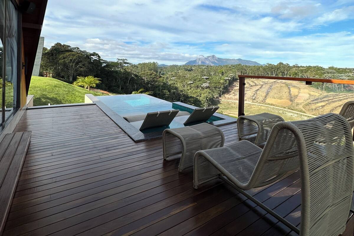 A wooden deck with lounge chairs and a pool, overlooking a mountainous landscape.