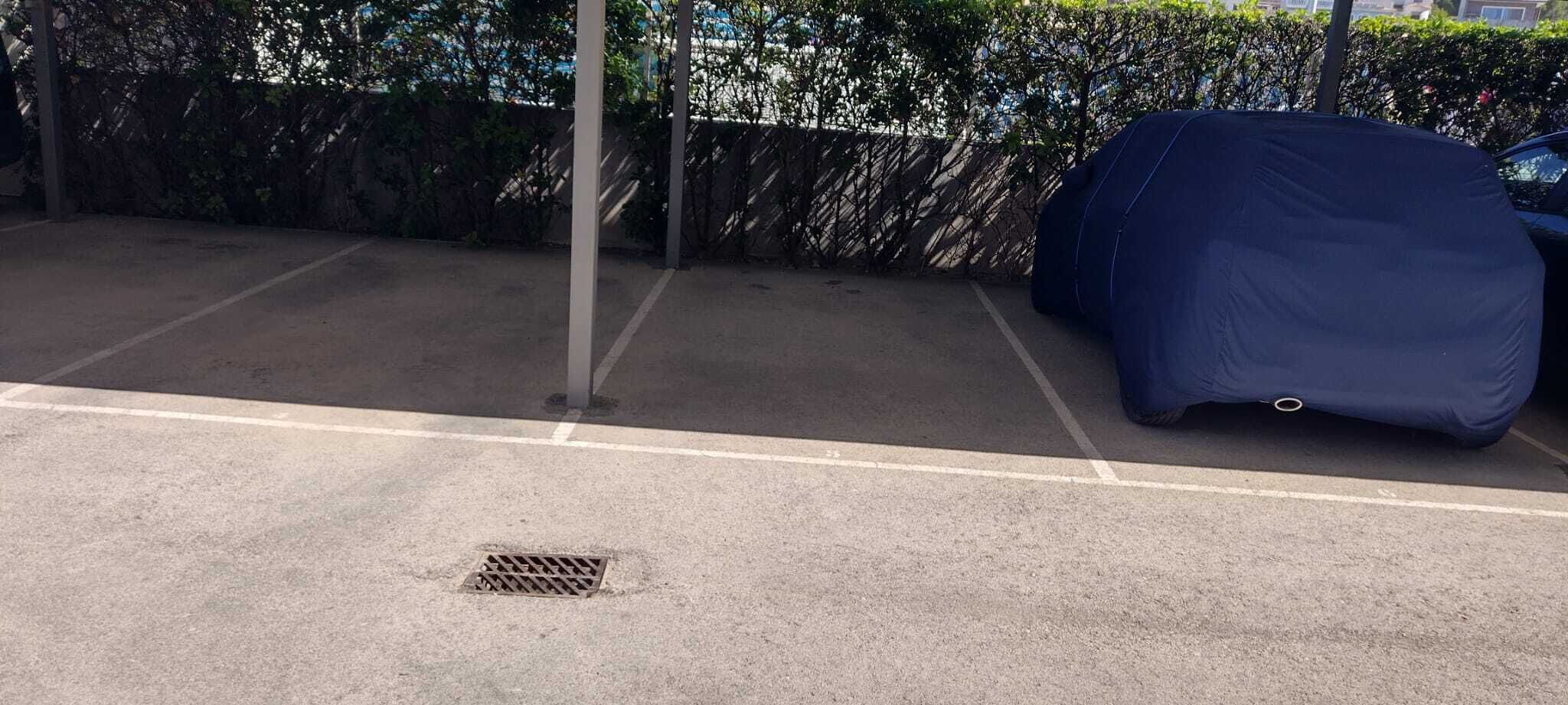 Un espace de stationnement abrité, avec une grille métallique et une clôture agrémentée de verdure.