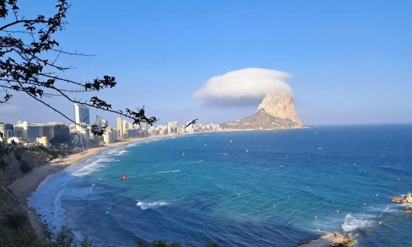 Eine Küstenlandschaft mit einem markanten Berg, blauem Himmel und einem Strand.