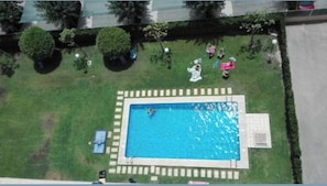 Vista aérea de una piscina rodeada por un césped cuidado y árboles.