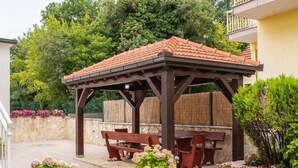 A covered outdoor seating area with benches and tables, surrounded by potted plants and a stone wall. - Apartment in Imotski near Lakeside Bliss (imotski)