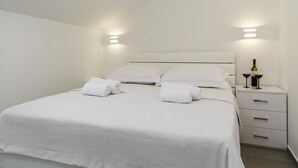 A modern hotel room with a neatly made bed, white linens, and a nightstand with a bottle and glasses. - Apartment in Imotski near Lakeside Bliss (imotski)