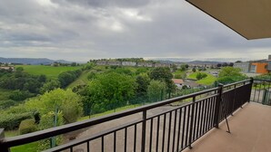Ein Balkon mit Blick auf eine grüne Landschaft, Gebäude und ferne Berge.