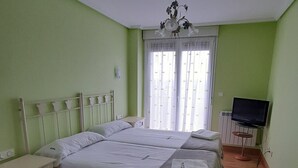 Ein Schlafzimmer mit einem großen Bett, Nachttischen, einem Fernseher und einem Fenster mit Vorhängen.