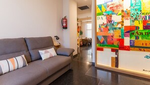 Uma sala de estar moderna com um sofá cinza, um extintor de incêndio na parede e uma obra de arte abstrata colorida.