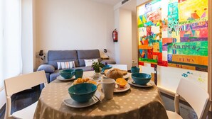 Uma sala de jantar com mesa posta para o café da manhã, um sofá ao fundo e um quadro abstrato colorido na parede.