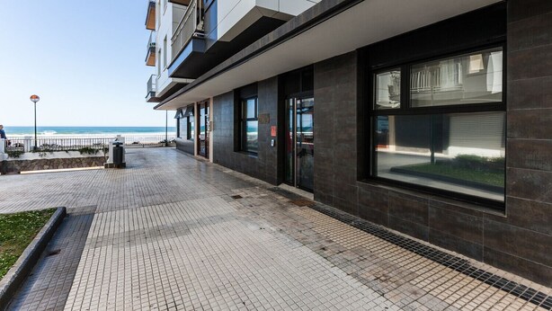 Un bâtiment moderne doté de grandes fenêtres, d’une allée pavée et offrant une vue sur la mer.