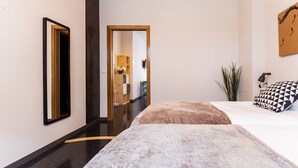 Une chambre d’hôtel moderne avec un grand lit, une porte en bois donnant sur la salle de bain et une petite plante près de la fenêtre.