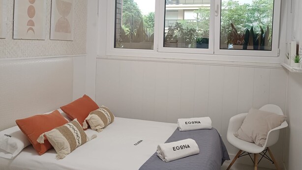 A bedroom with a bed, a chair, and a window with a view of greenery. - Apartment Frida - Nice, 150m from the beach by Egona (Zarautz)