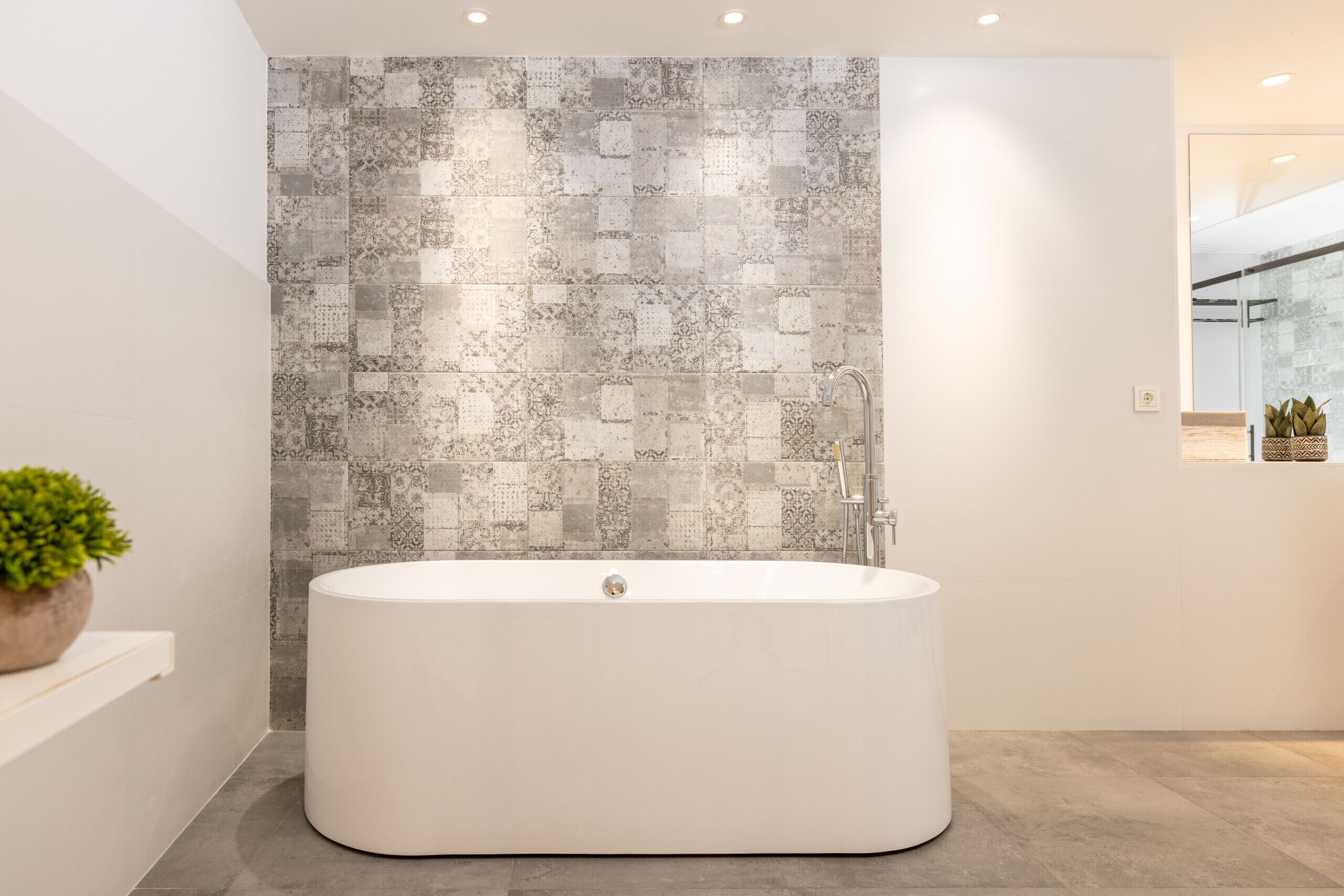 A modern bathroom with a freestanding bathtub, a textured wall, and a potted plant.