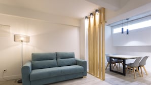 Een moderne woonkamer met een bank, een eettafel met stoelen, een vloerlamp en een houten scheidingswand.
