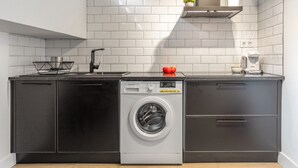 Een compacte keuken met een ingebouwde wasmachine en droger, een spoelbak en een koffiezetapparaat.