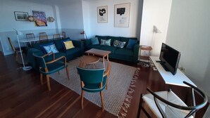A living room with a green sofa, wooden chairs, a coffee table, and a TV on a stand. - Apartment Muskaria - Spectacular, first line beach and pool by Egona (Zarautz)