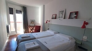 A hotel room with two beds, a desk, a chair, and a window with curtains. - Apartment Muskaria - Spectacular, first line beach and pool by Egona (Zarautz)