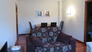 A living room with a sofa, a dining table with chairs, and two framed pictures on the wall. - Zinkunegi Apartment - Accommodation near the beach with parking by Egona (Zarautz)