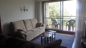 A living room with a sofa, a coffee table, and a view of a balcony with chairs and a table. - Zinkunegi Apartment - Accommodation near the beach with parking by Egona (Zarautz)