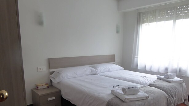 A hotel room with two beds, a bedside table, and a window with curtains. - Zinkunegi Apartment - Accommodation near the beach with parking by Egona (Zarautz)