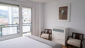 Een slaapkamer met een groot bed, twee stoelen, een kaptafel en uitzicht op de stad.