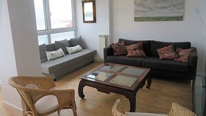 Een woonkamer met een bank, twee fauteuils, een salontafel en een schilderij aan de muur.