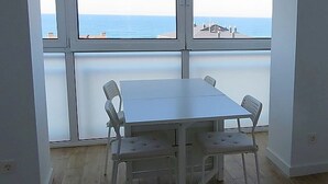 Een kamer met een groot raam met uitzicht op de zee, een witte tafel met vier stoelen en houten vloeren.