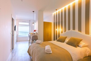 A hotel room with a large bed, a desk with a chair, and a view of the sea through a window. - Hondar apartment by Egona (Getaria)