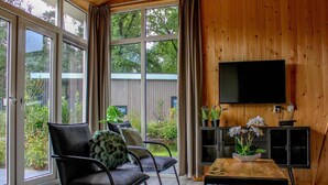 A modern living room with a large TV, comfortable seating, and a view of the outdoors. - Chic Chalet in Hoenderloo (Hoenderloo)