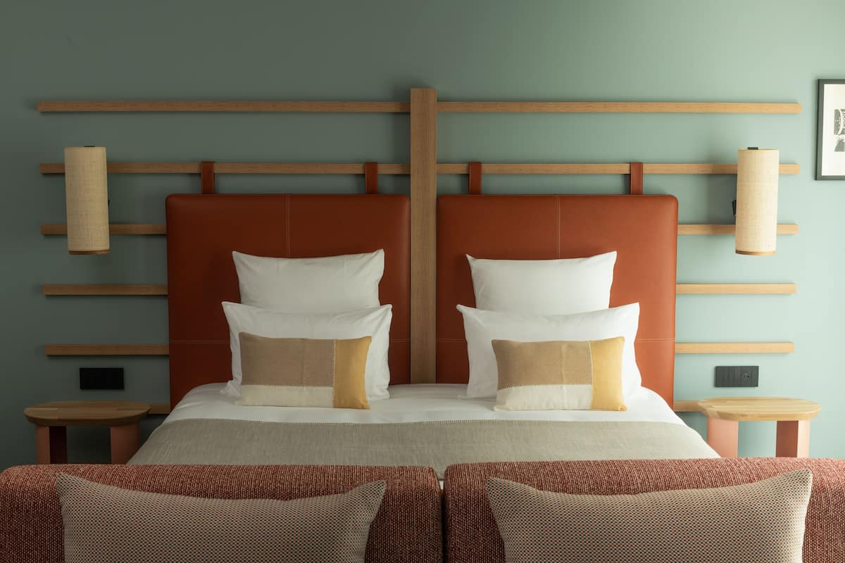 Ein ordentlich eingerichtetes Hotelzimmer mit einem großen Bett, zwei Nachttischen und einem Kopfteil mit horizontalen Holzleisten.