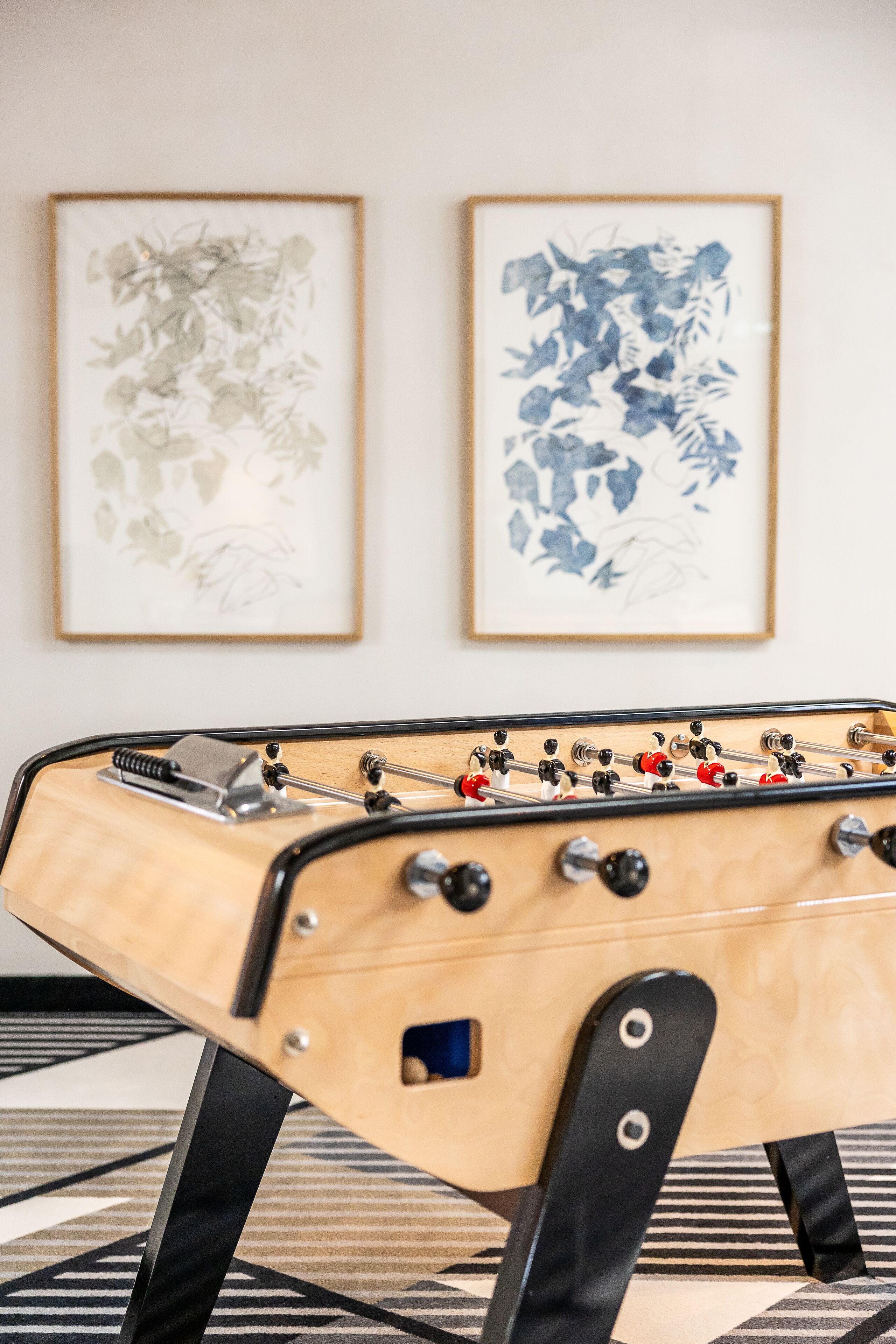 A foosball table in a room with two framed artworks on the wall.