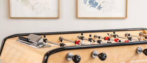 A foosball table in a room with two framed artworks on the wall.