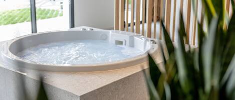 A hot tub with a view of a garden and a building in the background.