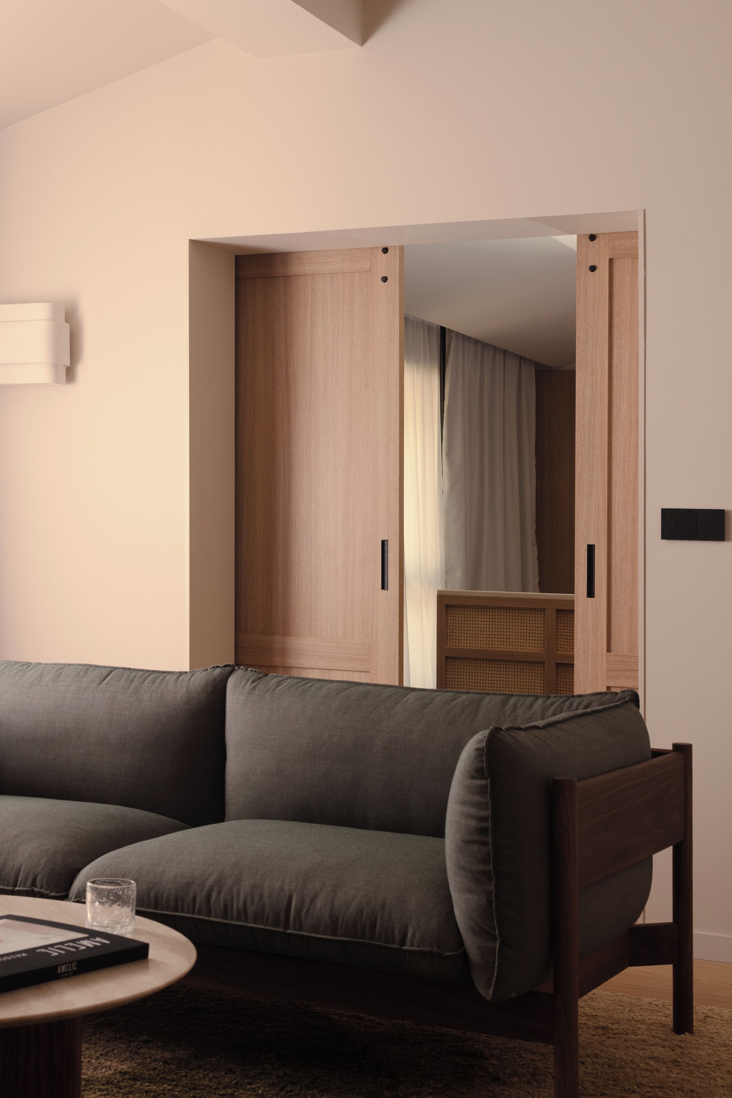 Un soggiorno moderno con un divano verde scuro, un tavolino da caffè e un armadio in legno con specchio.