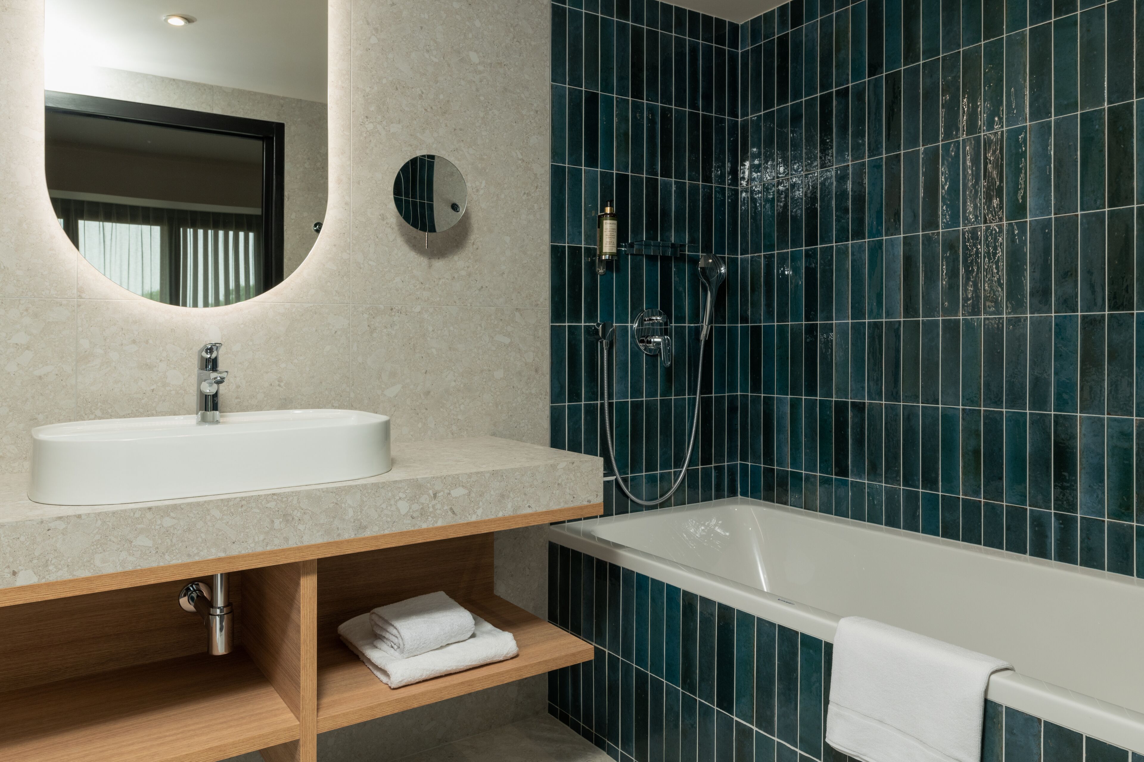 A modern bathroom with a white sink, a round mirror, a bathtub, and blue-tiled walls.