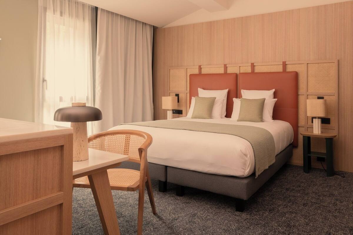 Ein Hotelzimmer mit einem Bett, einem Schreibtisch, einem Stuhl und zwei Nachttischen mit Lampen.
