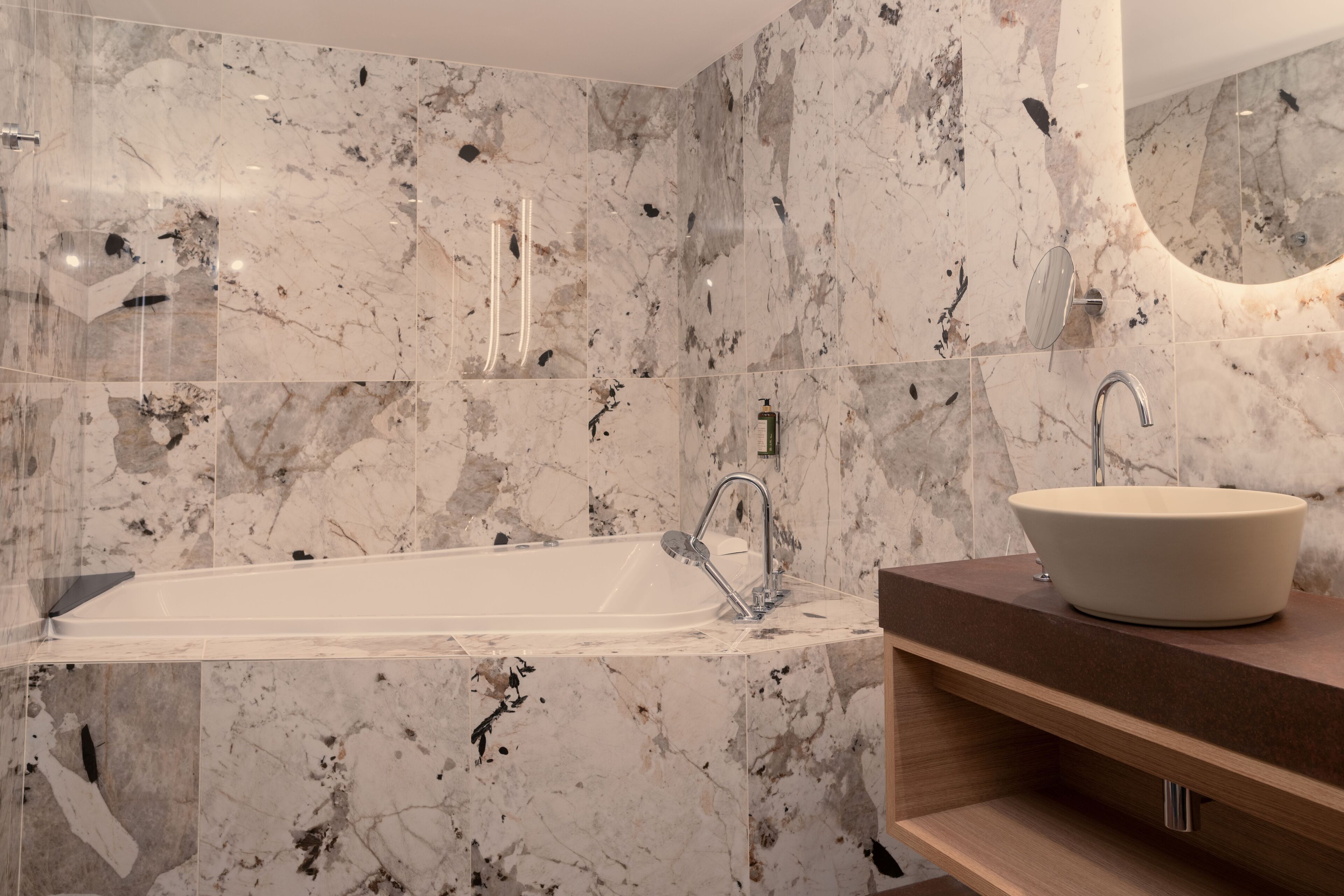 A modern bathroom with a freestanding bathtub, a vessel sink, and marble walls.