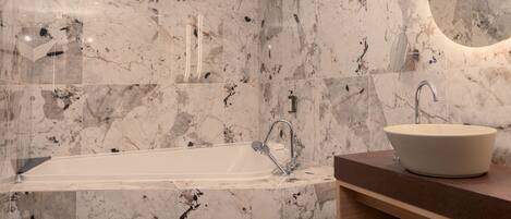 A modern bathroom with a freestanding bathtub, a vessel sink, and marble walls.