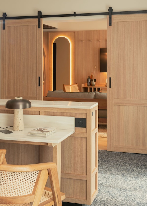 Un interior moderno con un escritorio de madera, una silla y un sofá. Hay una puerta corredera que da a un comedor.